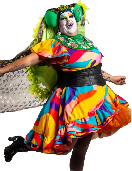 A Fourth City Sister of the Abbey of the Glittering Arch, a drag nun in whiteface makeup and a green wig, wearing a vibrant rainbow patchwork ruffled dress and posing mid-spin.